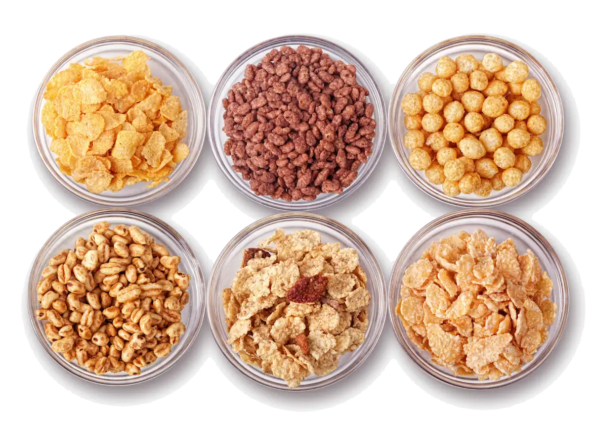 Six glass bowls filled with various types of breakfast cereals are arranged in two rows of three. The cereals include corn flakes, chocolate-flavored puffs, round corn puffs, crunchy wheat puffs, granola with dried fruit, and bran flakes.