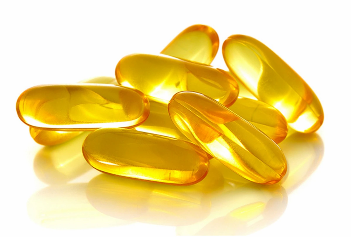 Close-up of several yellowish-golden translucent gel capsules, commonly used for dietary supplements or medication, clustered together on a white background. Light reflects off their smooth, shiny surfaces, enhancing their glossy appearance.